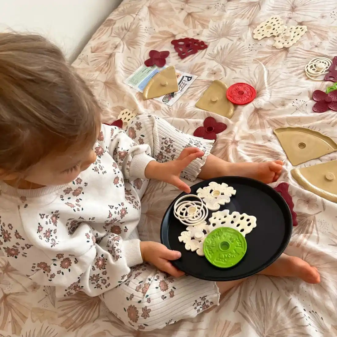 Copil care asamblează pizza Woopie pe tavă neagră, cu toppinguri și ingrediente de jucărie.