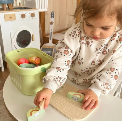 Copil care taie avocado din lemn Tooky Toy pe tocător, cu coșul de alimente aproape pentru joc de rol.