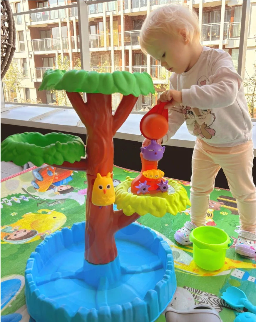 Copil care toarnă apă în copacul Woopie Big Tree Water Table, activând roțile și traseele de apă.