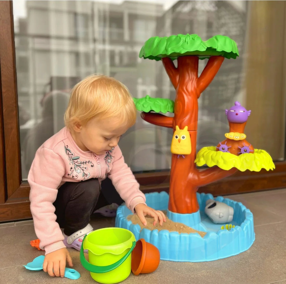 Copil care se joacă la masa Woopie Big Tree Water Table, cu găletușă, lopățică și bazin pentru nisip.
