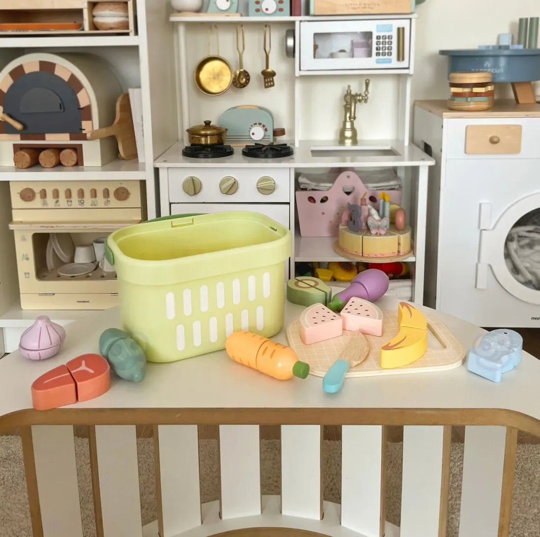 Set Tooky Toy cu coș și alimente din lemn așezate într-o bucătărie de joacă, pentru scenarii de gătit.