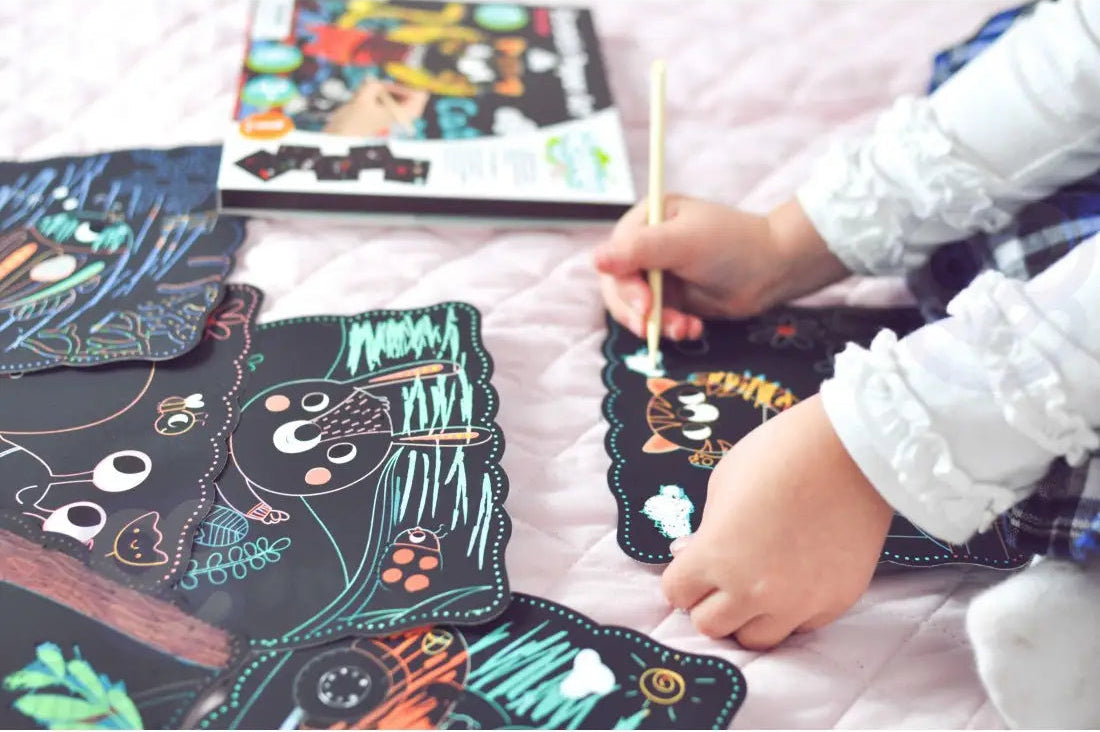 Copil care deseneaza prin razuire pe plansele Woopie Scratch Art, cu ambalajul in fundal.