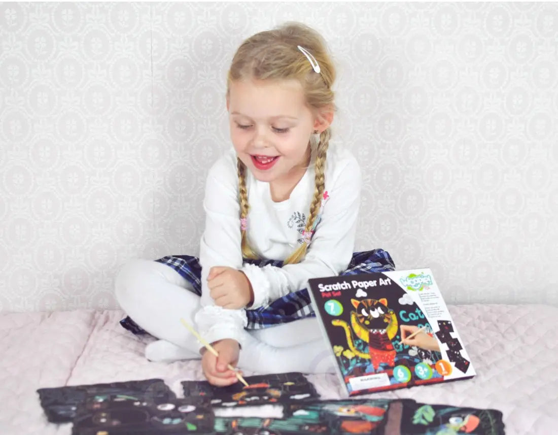 Copil vesel care se joaca cu setul Woopie Scratch Paper Art Pet Set.