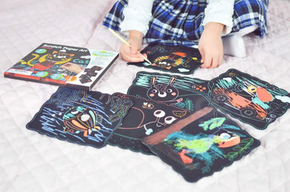 Planse Woopie Scratch Art colorate prin razuire, asezate pe pat langa cutia produsului.