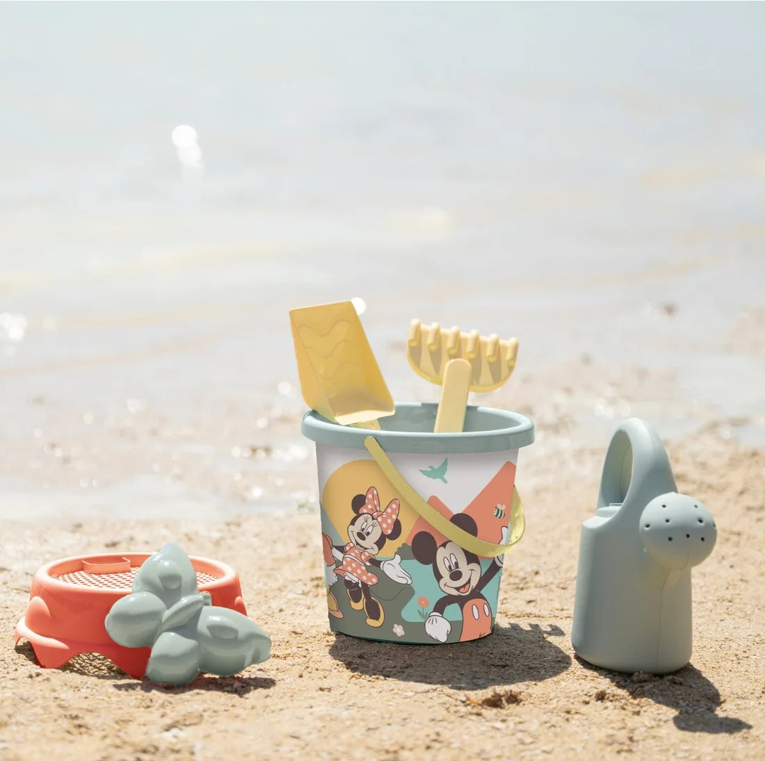 Setul Smoby Life Mickey și Minnie așezat pe nisip, cu găletușă, stropitoare și accesorii pentru joacă la plajă.