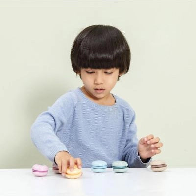 Copil care atinge un macaron galben PolarB Viga și sortează piesele colorate pe masă.