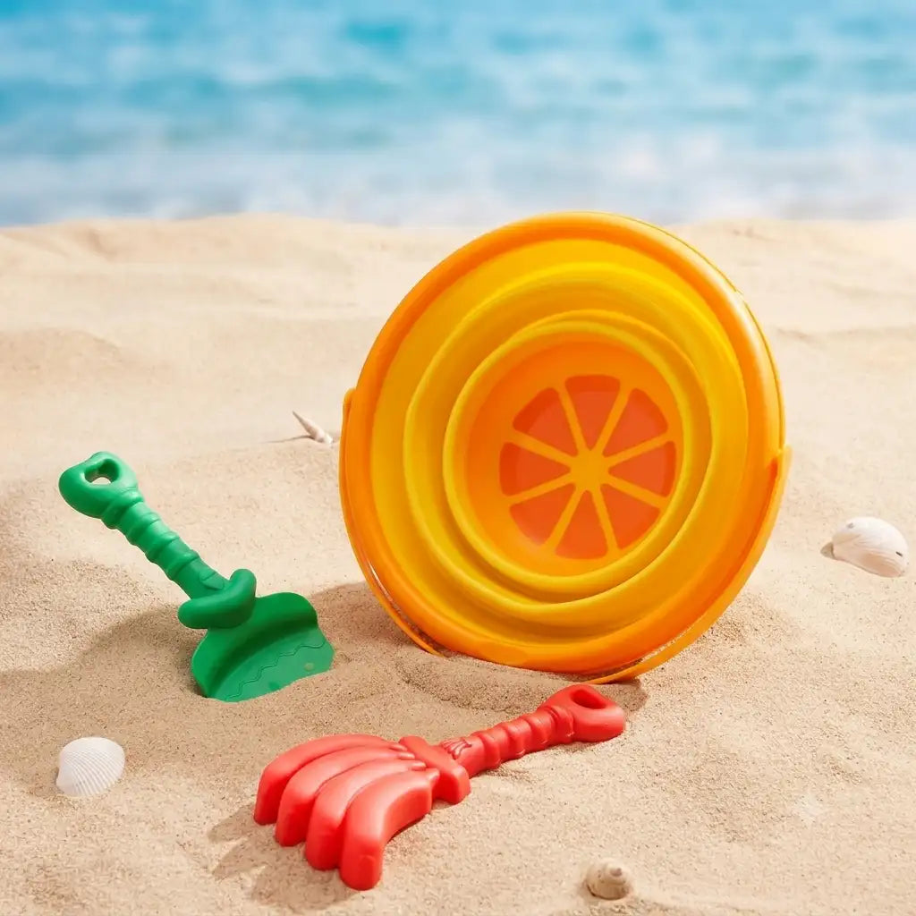 Set Woopie Tropical Fruits pentru vacanță, așezat pe plajă lângă geantă, prosop, papuci și scoici.