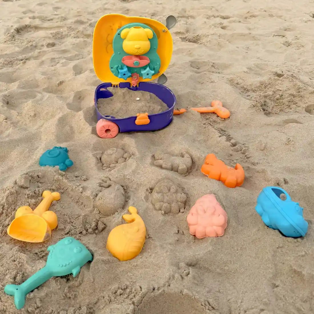 Set de nisip Woopie pe plajă, cu valiza Cățeluș deschisă și forme colorate în nisip.