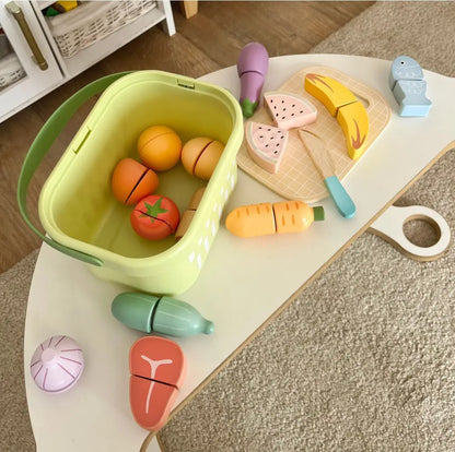 Set Tooky Toy cu fructe și legume din lemn aranjate pe masă, cu coș, tocător și piese de tăiat.